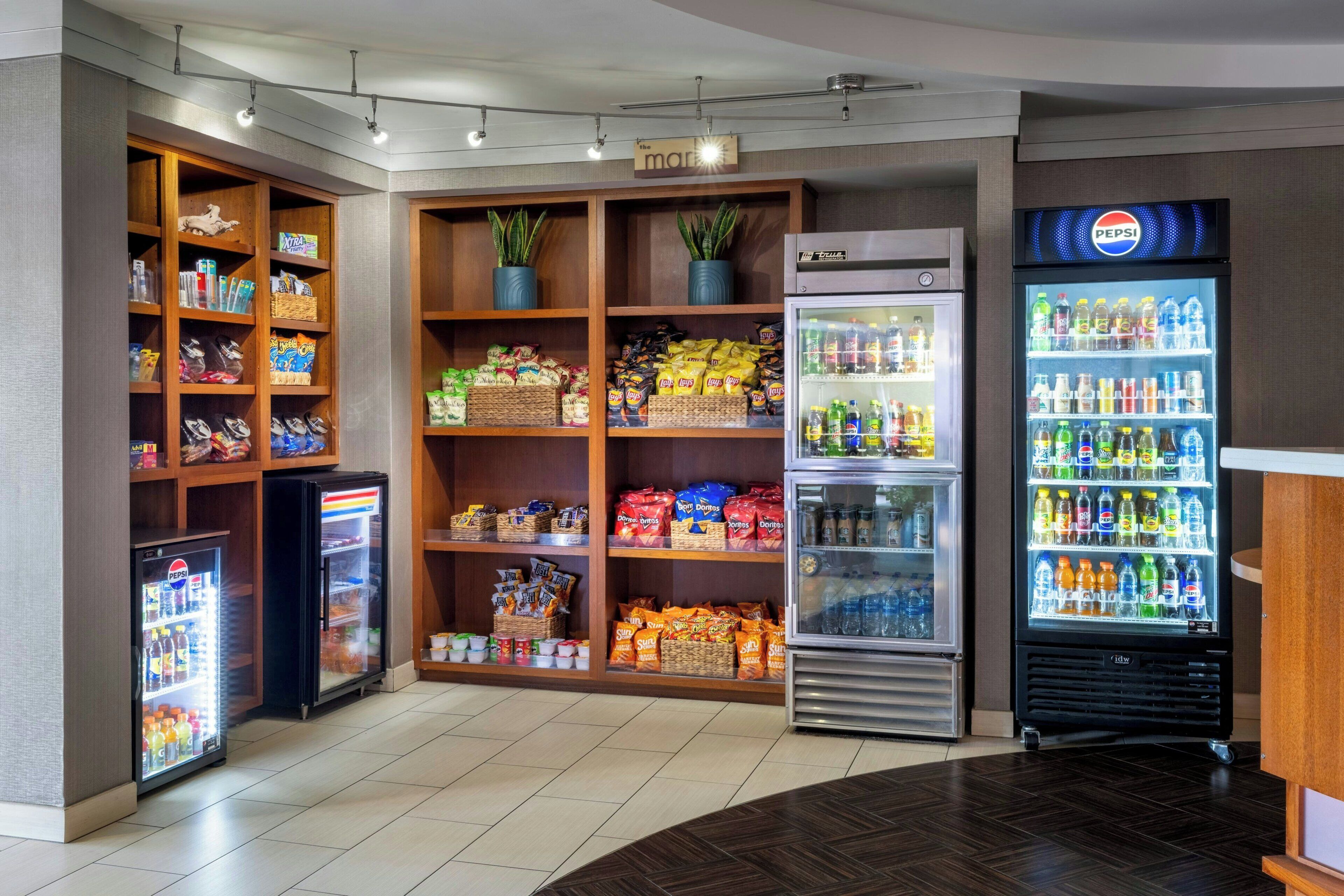 Un espace de libre-service où l’on peut se servir des boissons, notamment du Pepsi, avec un présentoir réfrigéré et des étagères remplies de collations et de boissons.