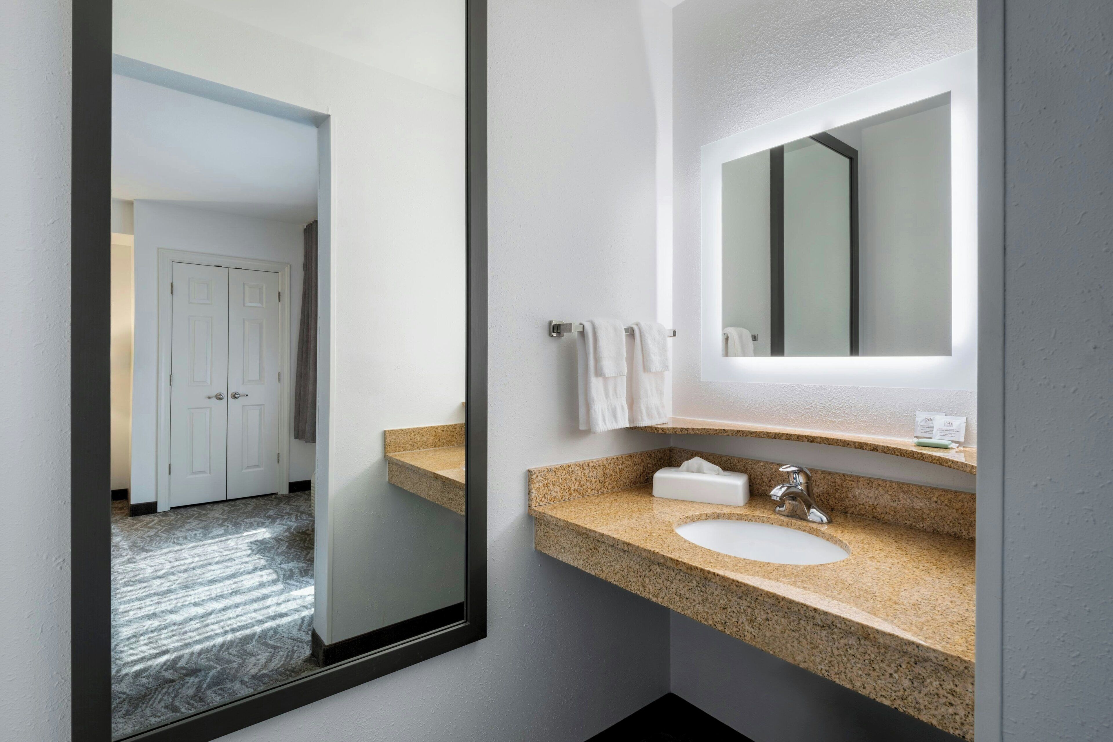 Casa de banho moderna com bancada de granito, uma pia, um espelho e uma porta que dá para outro quarto.
