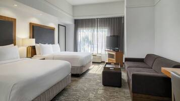 Ett hotellrum med två sängar, en soffa, en tv och ett fönster med gardiner.