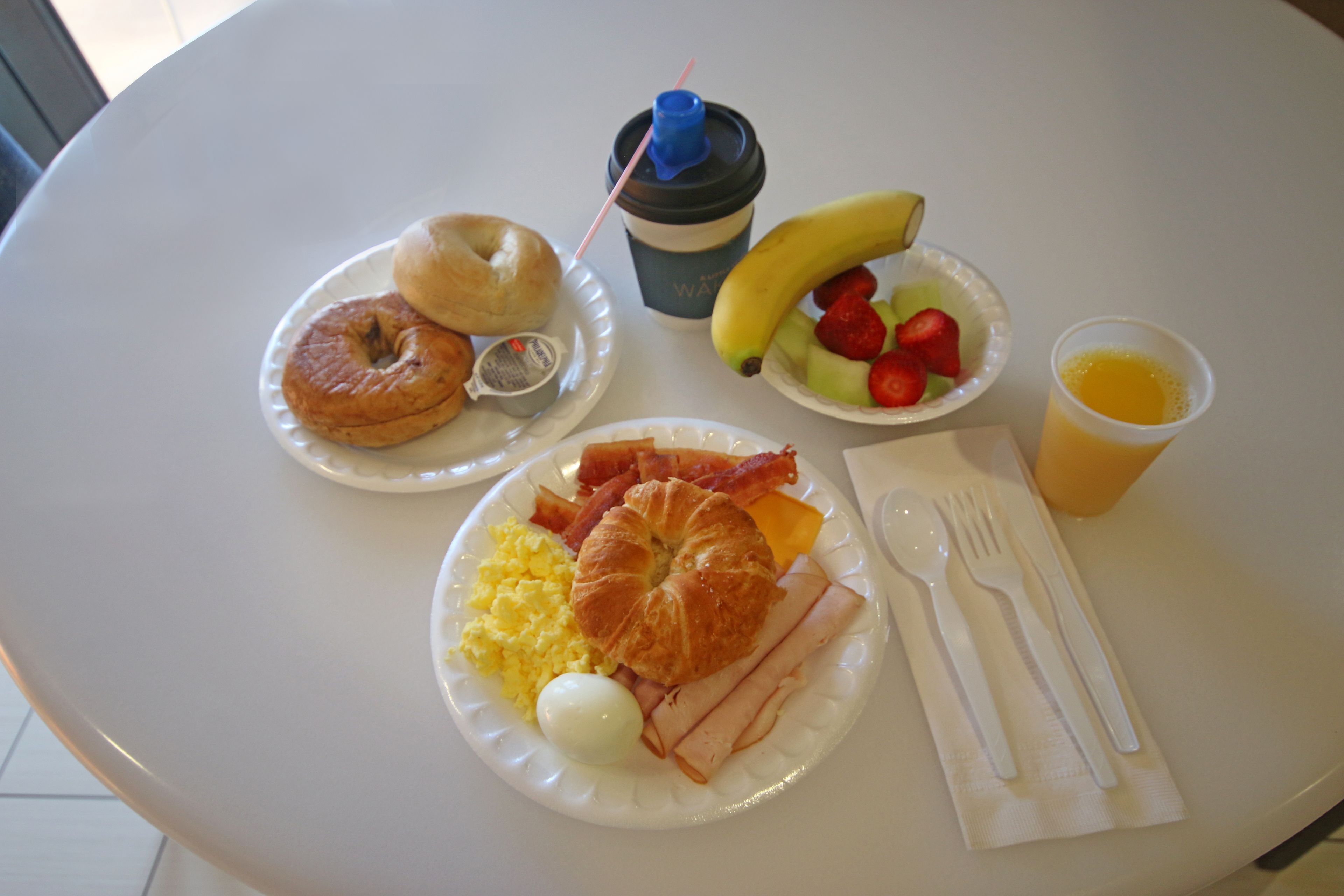 Un plato de desayuno con huevos, tocino, jamón, un croissant y un bagel.