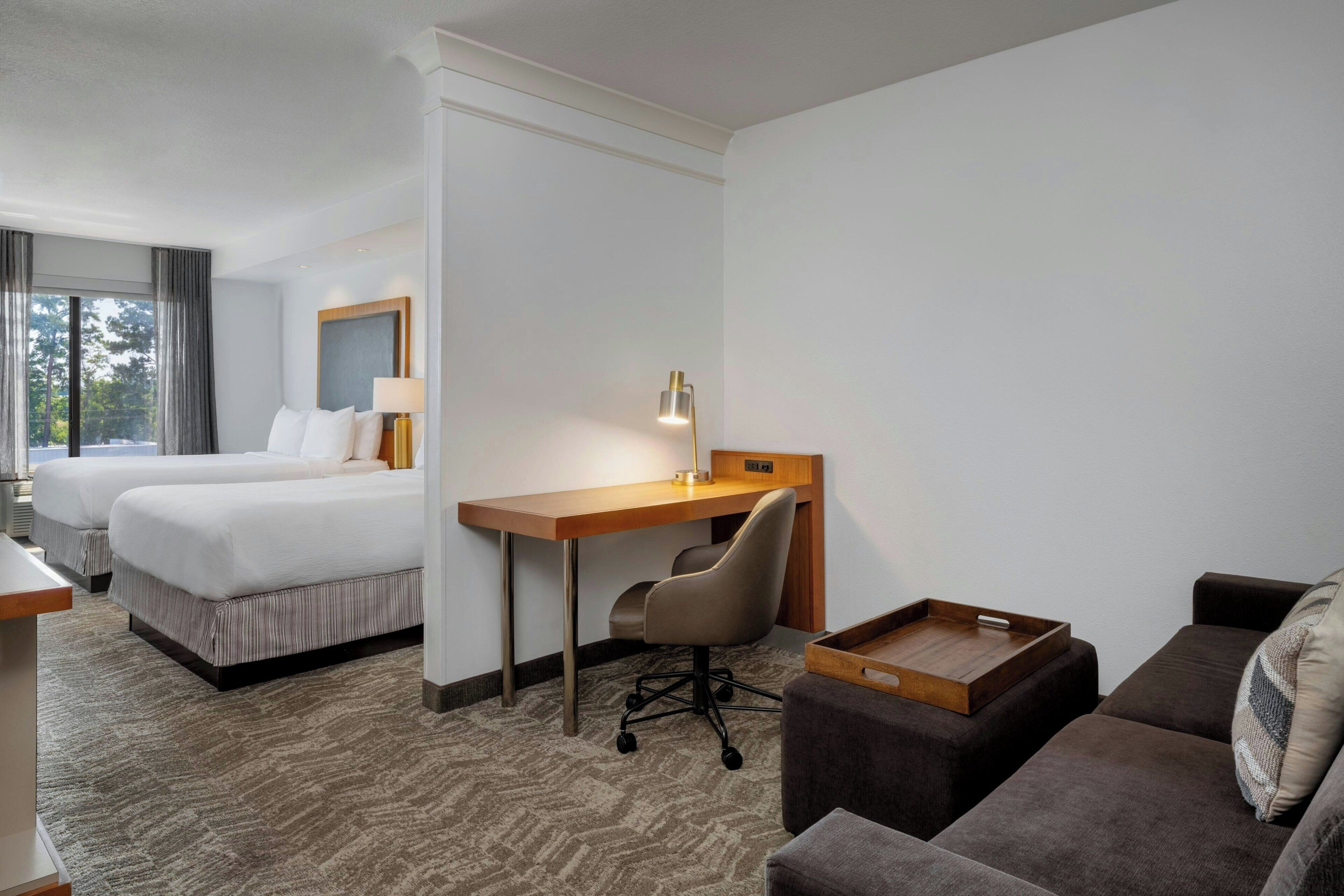 Habitación de hotel con dos camas, un escritorio, una silla, un sofá y una pequeña mesa de madera.