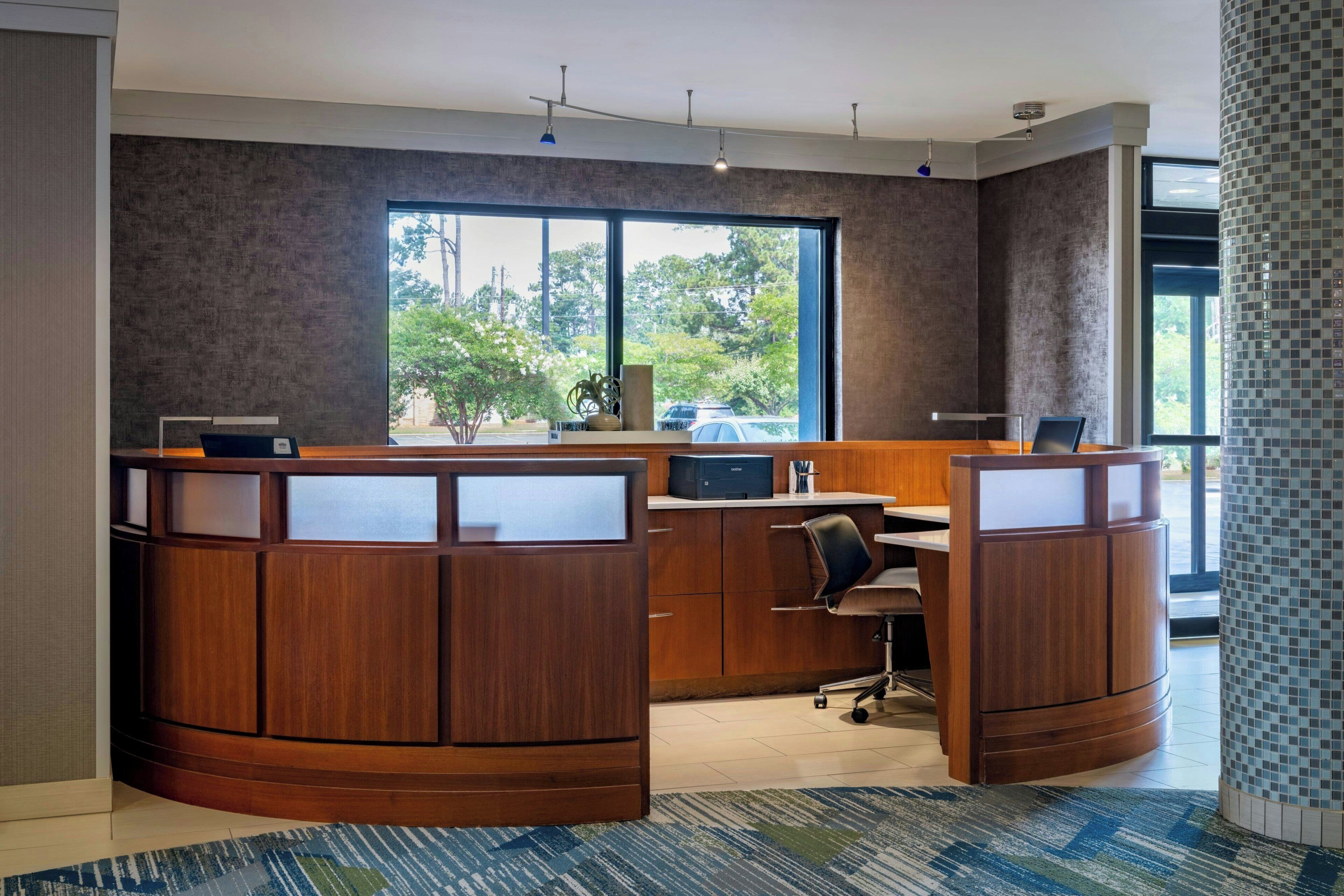 A modern reception desk with a large window, a wooden counter, and a seating area.