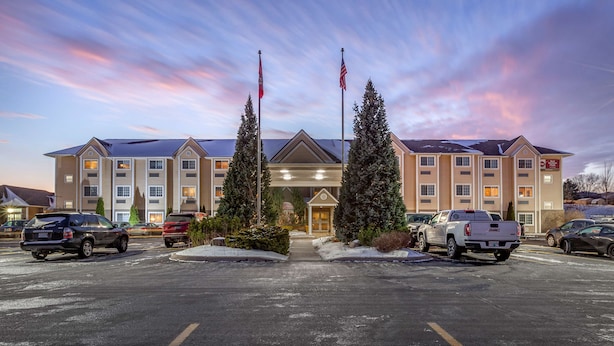 A hotel with a central entrance, multiple floors, and a parking lot with several vehicles.