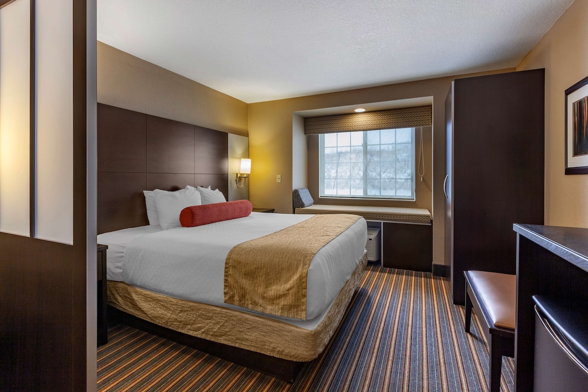 A hotel room with a large bed, a desk, a window with a view, and a bench.