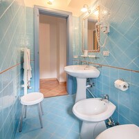 Un baño con azulejos azules, un lavamanos blanco, un inodoro y un espejo con toallero.