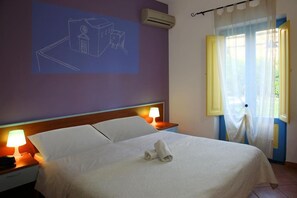 A hotel room with a bed, two bedside lamps, a wall-mounted air conditioner, and a window with curtains.