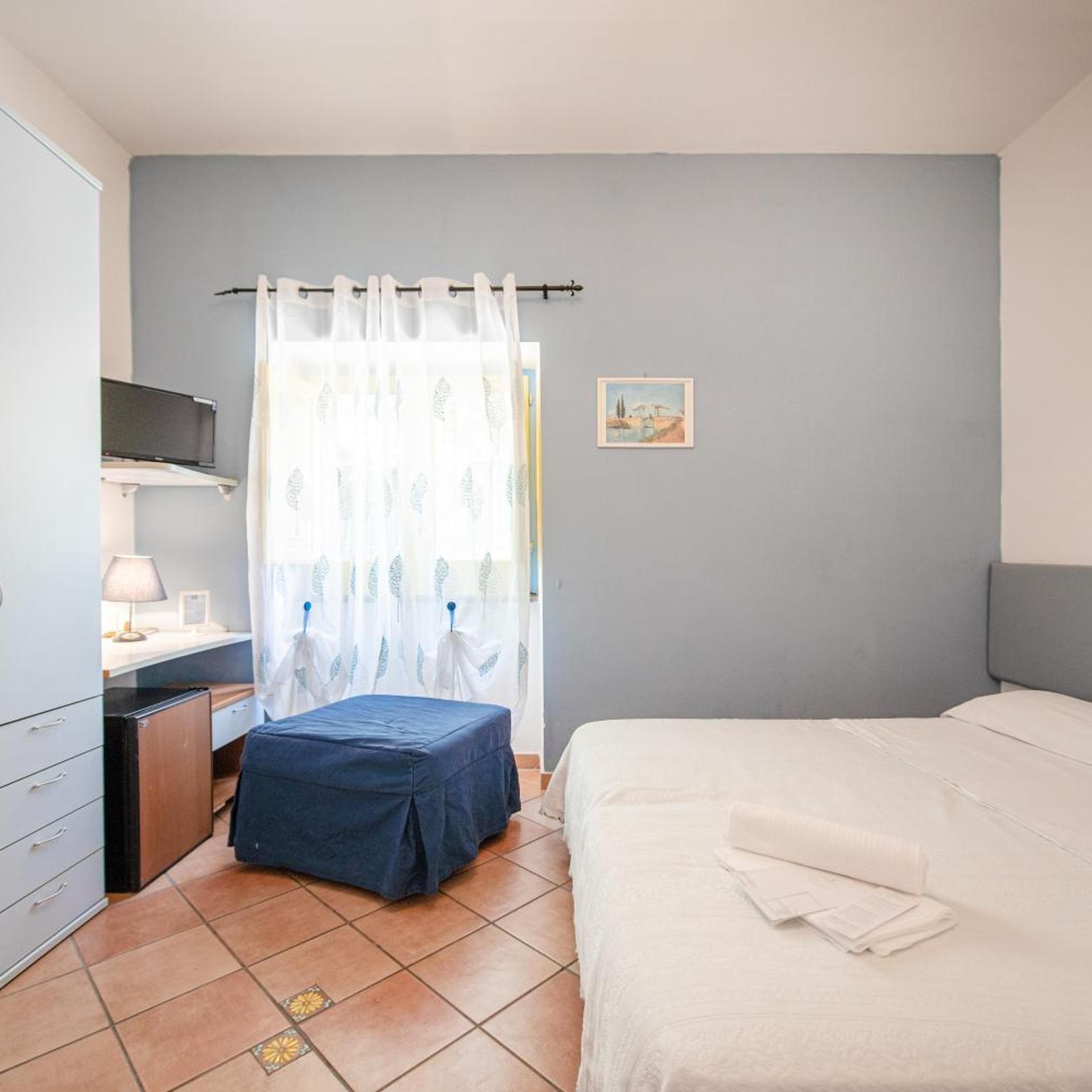 A bedroom with a bed, a desk, a chair, and a small cabinet.