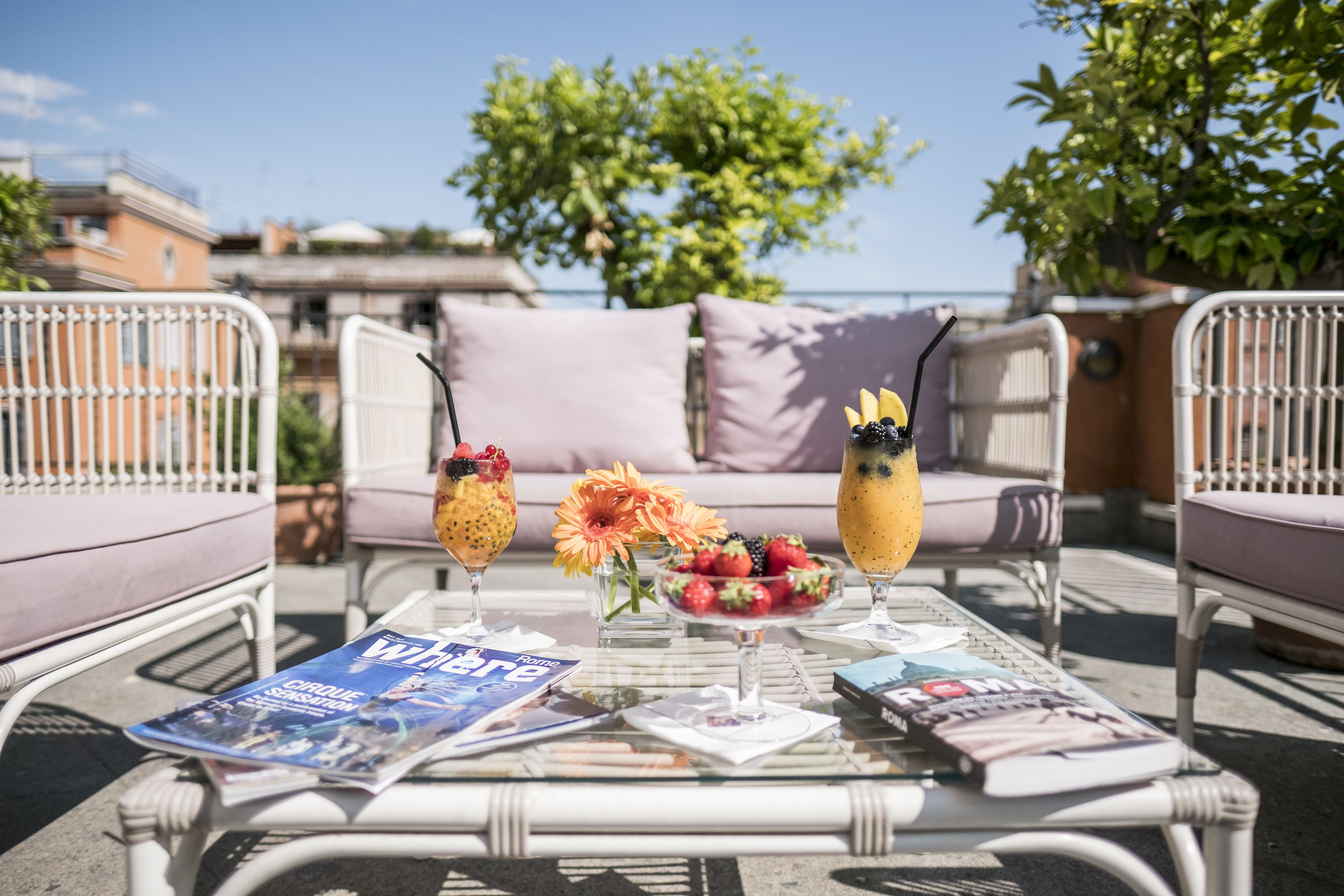 A wicker table with magazines, a fruit bowl, and two drinks.