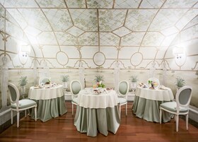 A dining area with round tables, green chairs, and a ceiling with a geometric pattern.
