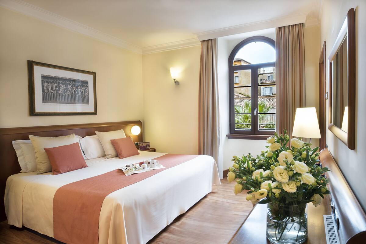 A hotel room with a bed, bedside table, lamp, and a window with curtains.