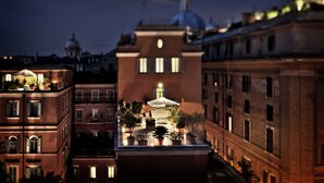 A rooftop terrace with potted plants and a table under an umbrella, overlooking a cityscape with historic buildings and domed structures. - Hotel Ponte Sisto (Rome)
