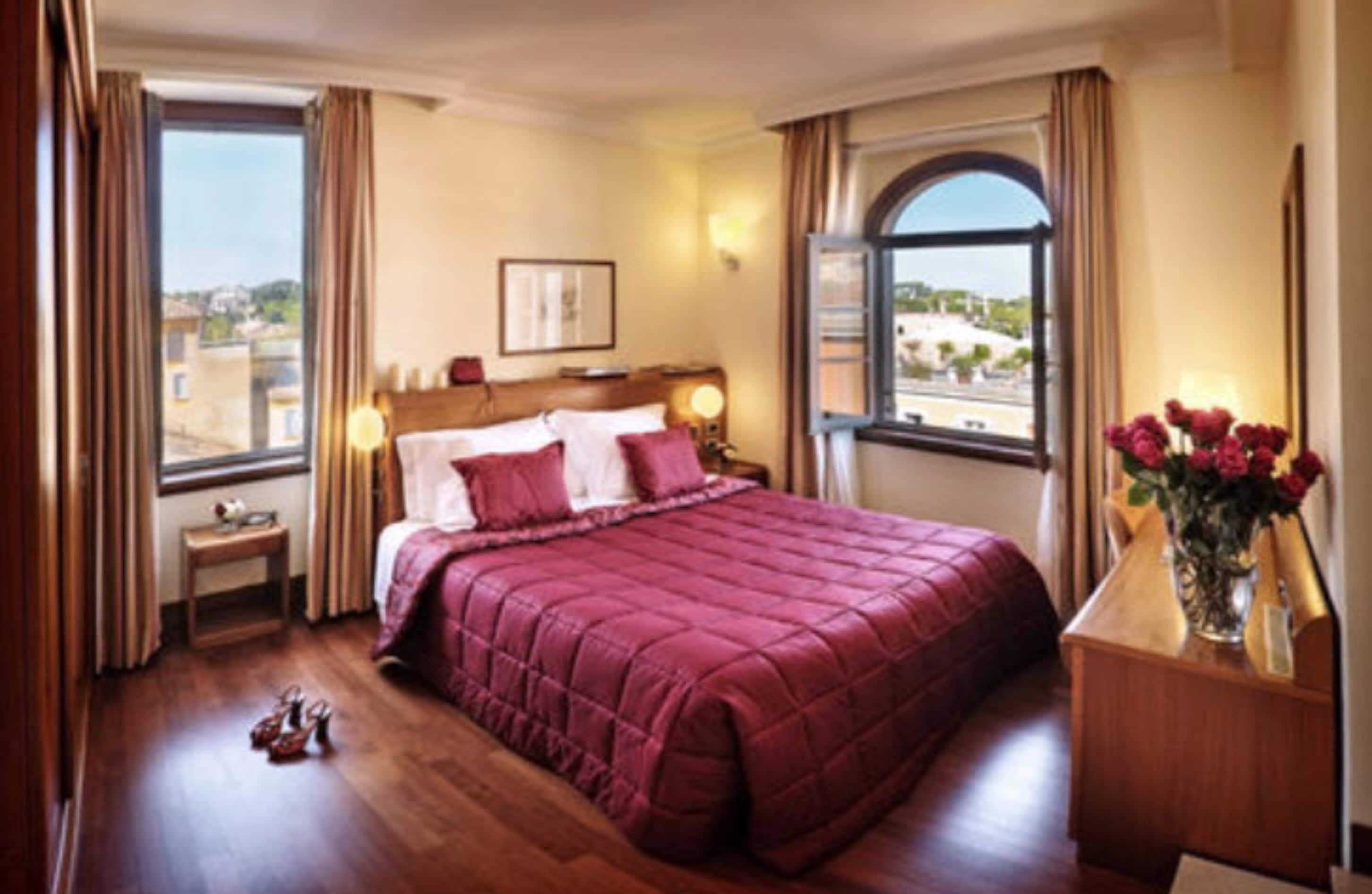 Habitación de hotel con una cama grande, una mesita de noche, un escritorio con un florero y una ventana con cortinas.