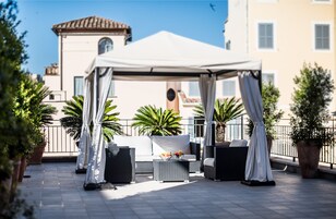 En udendørs terrasse med hvid markise, fletmøbler og krukker med planter.