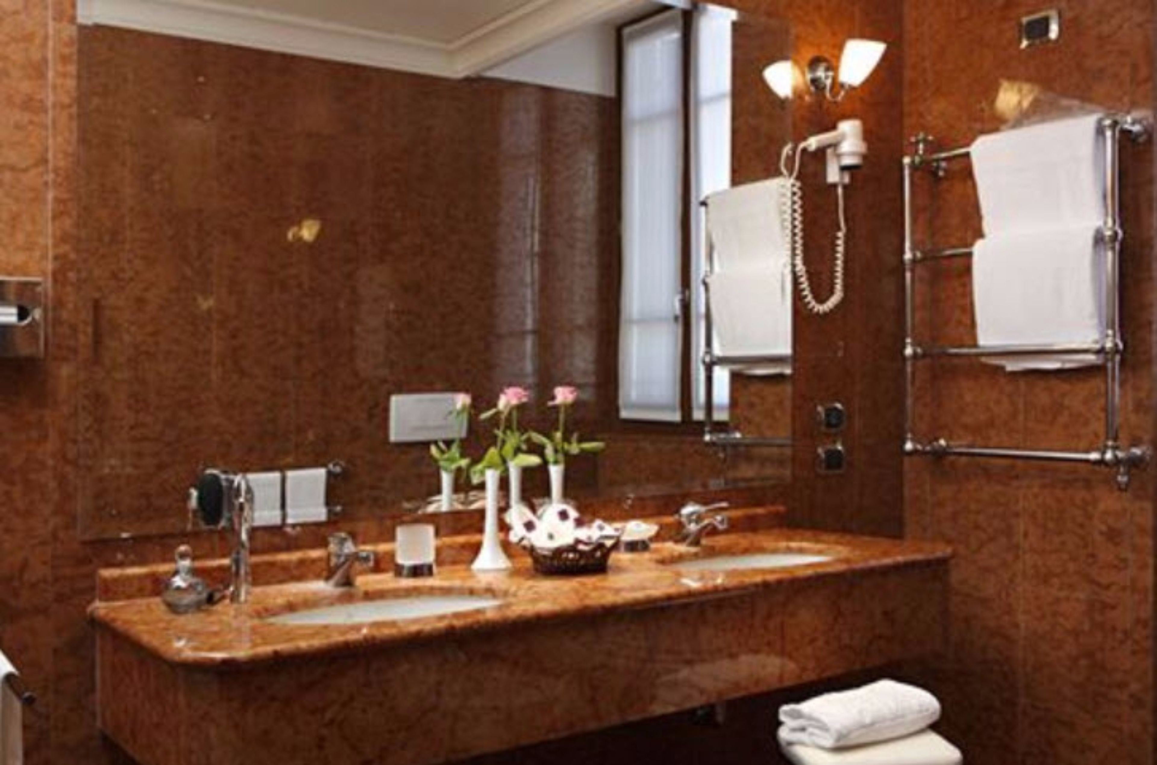 A bathroom with a marble countertop, two sinks, a mirror, a towel rack, and a shower area.