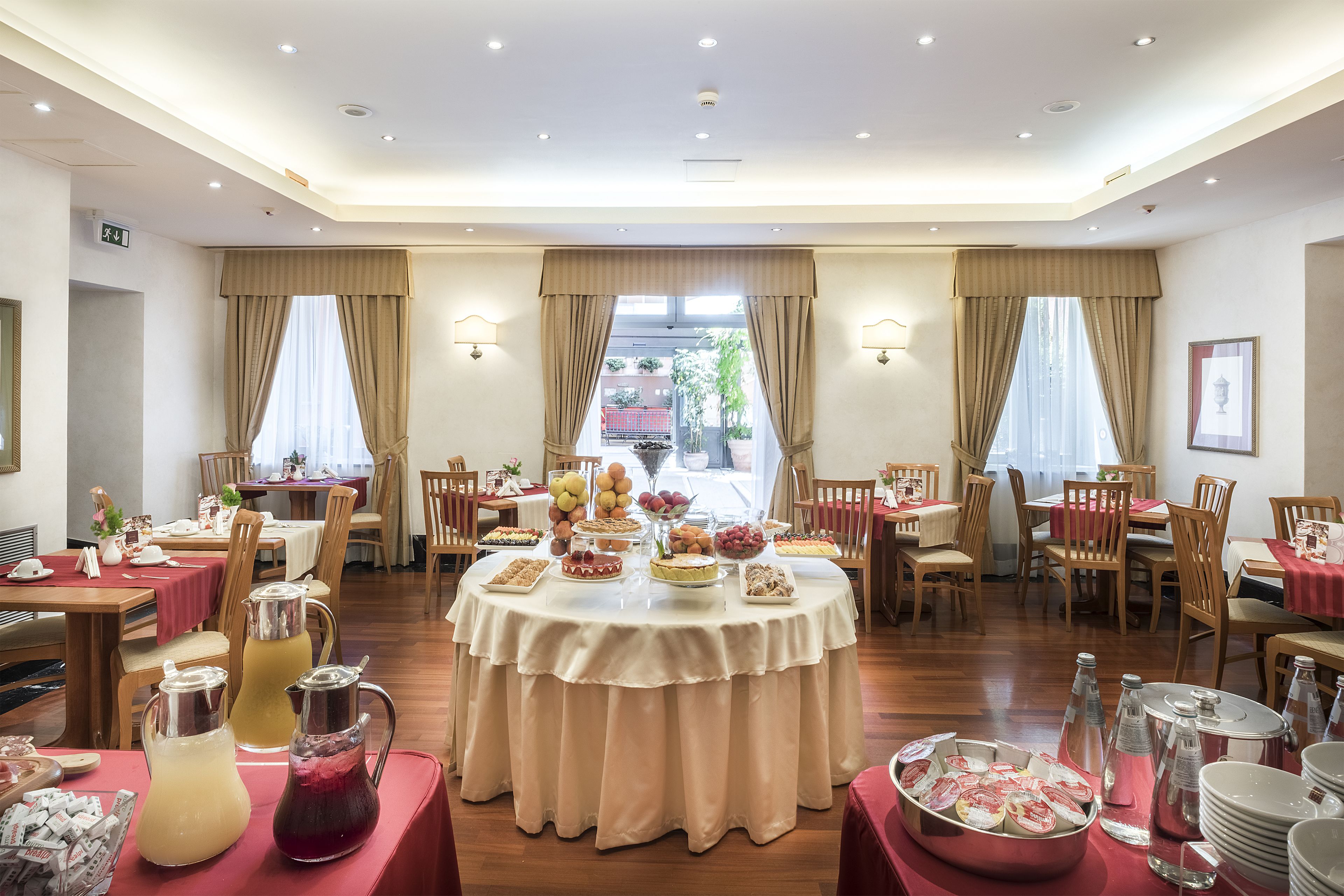 Un comedor amplio con mesas redondas, un sistema de buffet y vistas al exterior.