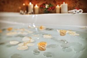 A bathtub with rose petals floating on the water, surrounded by candles and towels.