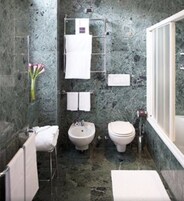 A bathroom with a marble wall, a bidet, a toilet, and a towel rack.