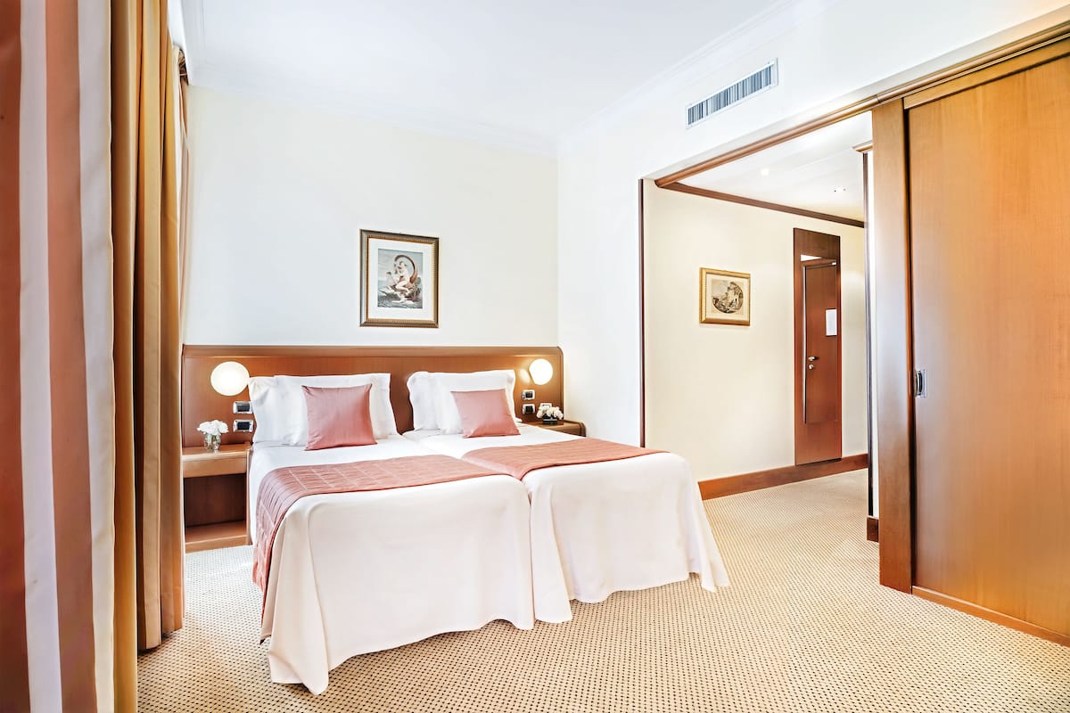 A hotel room with two beds, a wooden headboard, a nightstand with a lamp, and a framed picture on the wall.