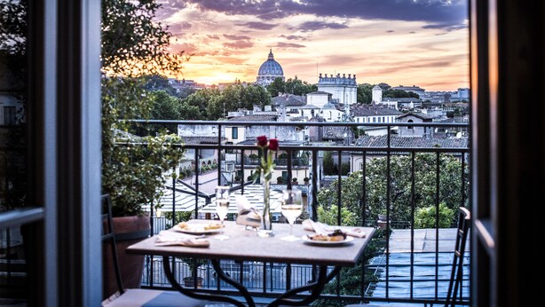 A balcony with a table set for dining, overlooking a cityscape with historic buildings and a prominent dome. - Hotel Ponte Sisto (Rome)