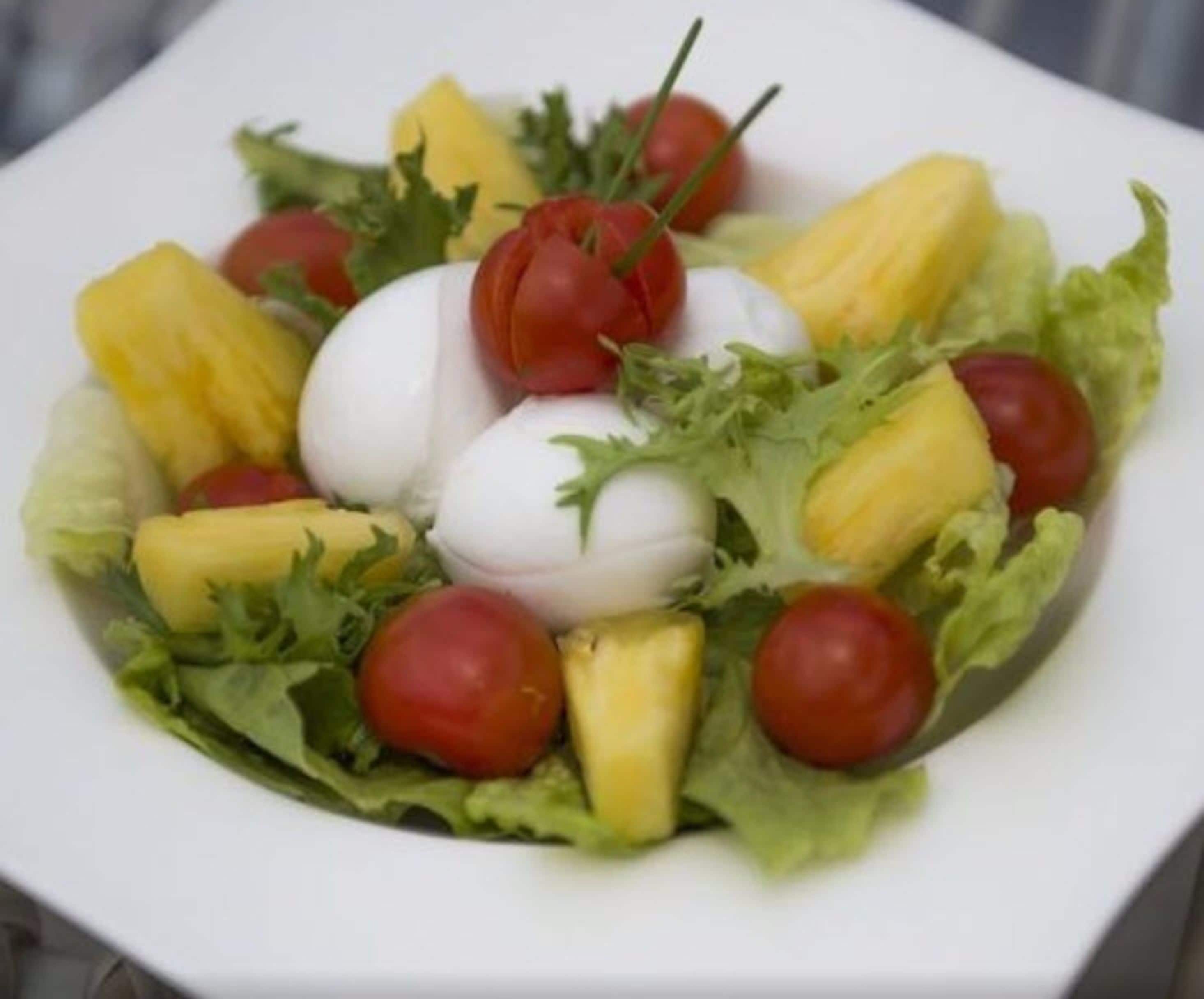 Ensalada con lechuga, tomates, piña y un huevo duro sobre un plato blanco.