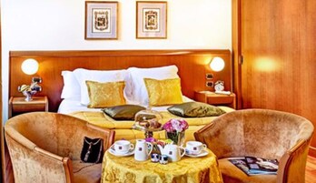 Ein Hotelzimmer mit einem großen Bett, zwei Nachttischen mit Lampen, einem kleinen Tisch mit Teetassen und zwei Sesseln.