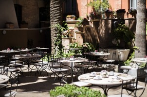 An outdoor café with round tables and chairs, surrounded by potted plants and a brick wall.