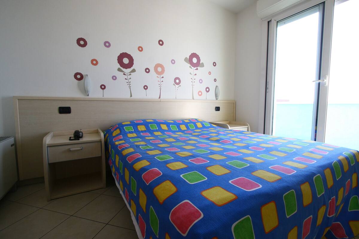 Une chambre à coucher comprenant un lit, une table de chevet, une commode et un mur décoré de motifs floraux.