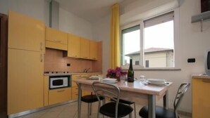 A compact kitchen with yellow cabinets, a dining table with four chairs, a window with a view, and a small oven. - Residence Beach Paradise (Rimini)