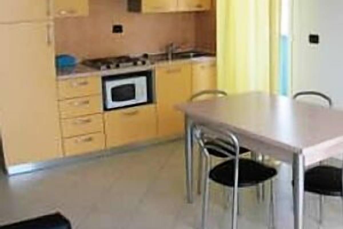 Une cuisine de taille réduite avec des meubles de couleur jaune, une cuisinière et une table à manger avec des chaises.