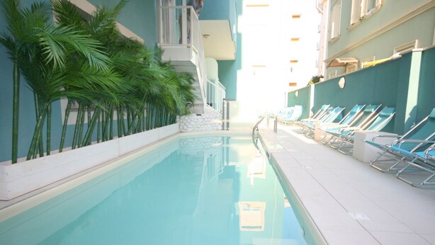 A swimming pool with a tiled edge, surrounded by lounge chairs and palm trees. - Residence Beach Paradise (Rimini)