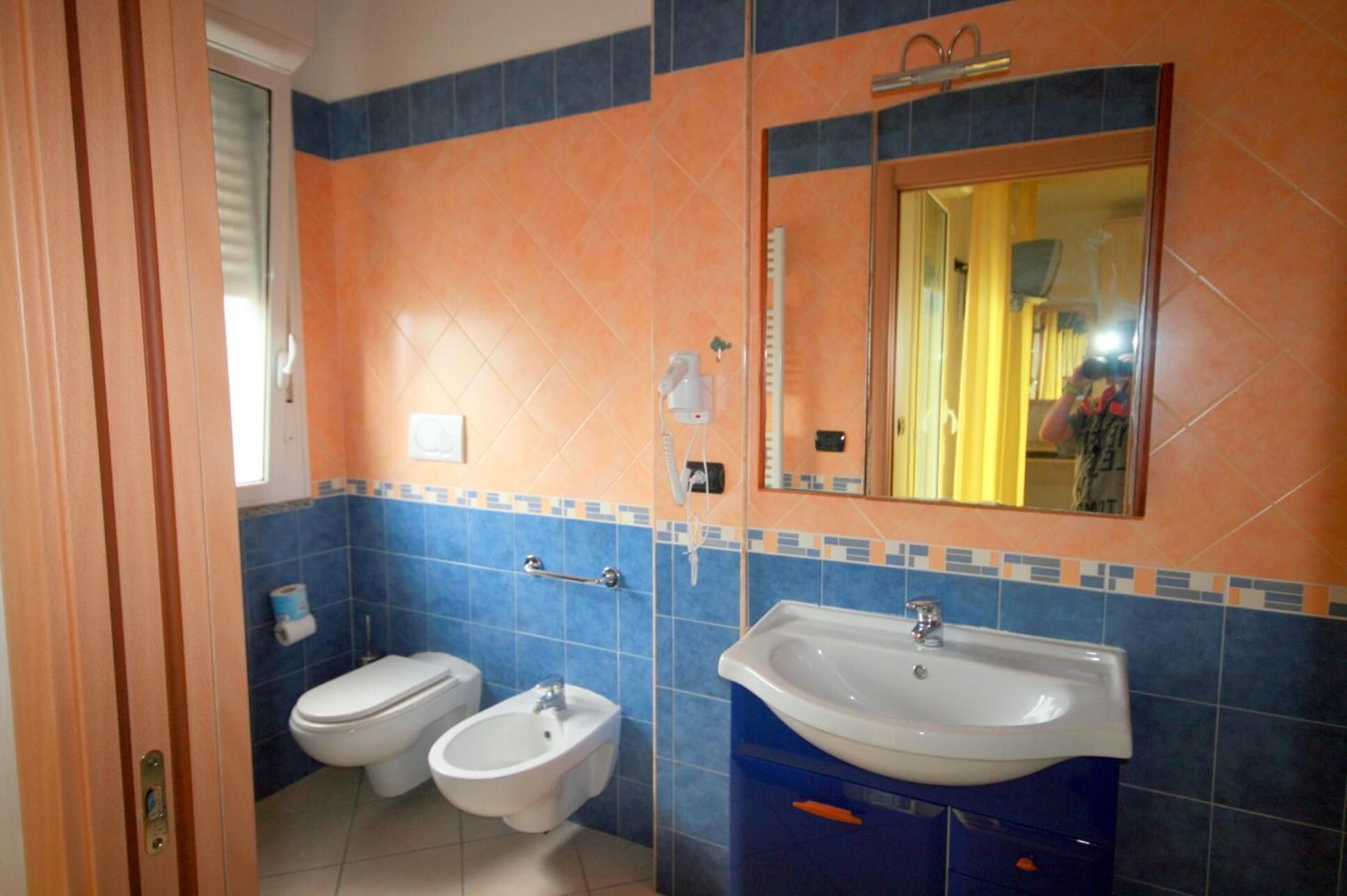 A bathroom with two toilets, a bidet, a sink, and a mirror.
