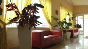 A spacious living room with a red leather sofa, large potted plants, and yellow curtains. - Residence Beach Paradise (Rimini)