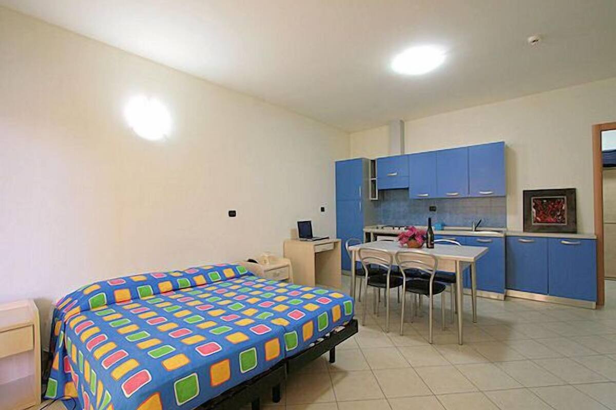 Une petite pièce bien éclairée, équipée d’un lit, d’un bureau et d’une kitchenette.