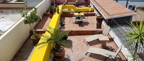 A rooftop patio with yellow barriers, potted plants, and outdoor furniture.