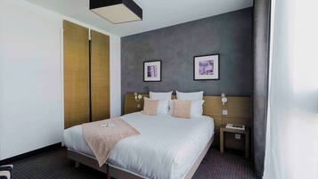 A modern hotel room with a large bed, a bedside table, a nightstand, and a wall-mounted lamp.