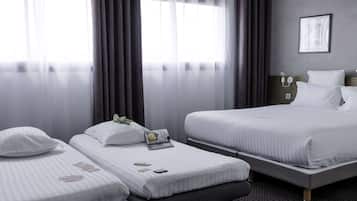 A hotel room with two single beds, a large bed, a bedside table with a lamp, a framed picture on the wall, and a window with curtains.