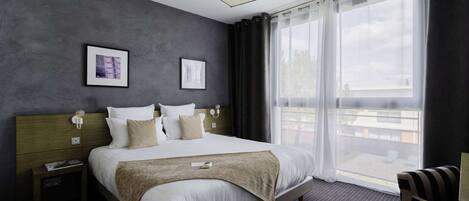 Habitación de hotel moderna con una cama grande, una mesita de noche, una silla y vistas al exterior a través de cortinas translúcidas.
