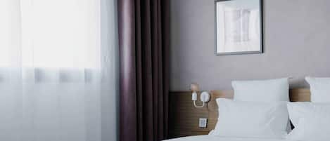 A neatly made bed with white linens, a wooden headboard, a bedside table with a lamp, and a framed picture on the wall.