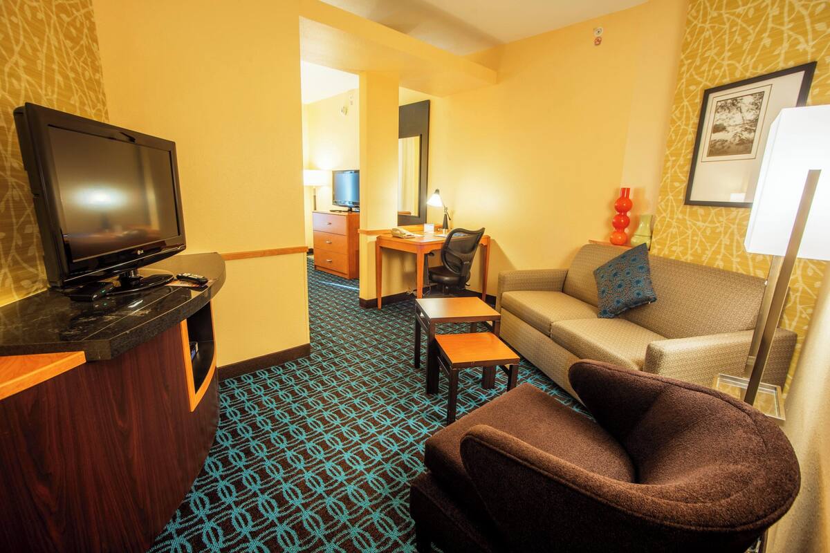 A hotel room with a TV, a sofa, a desk, and a patterned carpet.