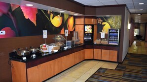 Un espace d’accueil d’hôtel doté d’un comptoir incurvé, d’une fresque murale sur le thème des fruits, d’un distributeur de boissons et d’un écran numérique affichant des informations.