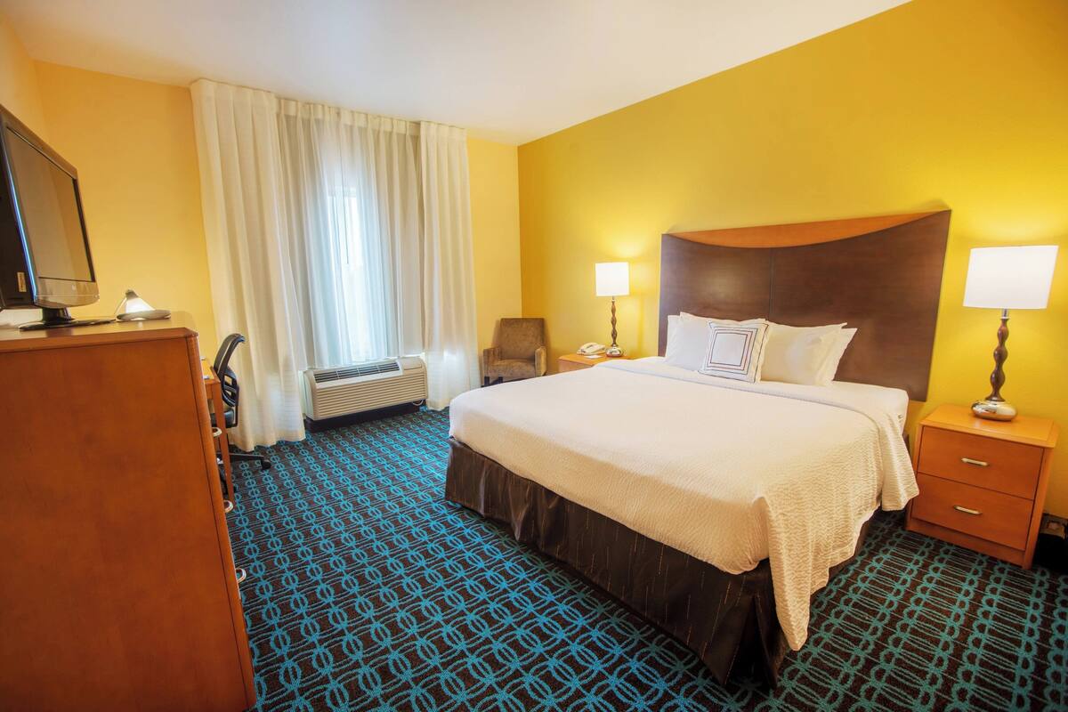 A hotel room with a large bed, bedside lamps, a desk with a computer, and a window with curtains.
