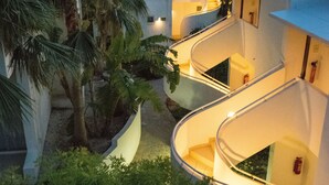 A modern hotel with curved balconies, palm trees, and a well-lit interior. - Theo Sunset Bay Hotel (Kissonerga)