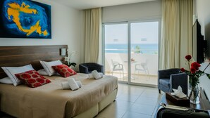 A hotel room with a bed, a desk with a vase of flowers, a chair, and a large window with a view of the sea. - Theo Sunset Bay Hotel (Kissonerga)