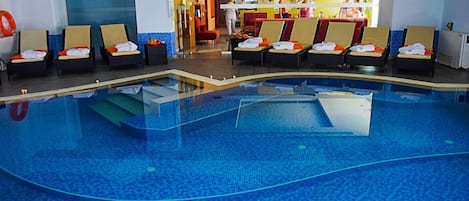 Piscina con sillas de descanso y toallas, una zona de recepción y un bar.
