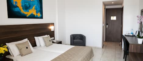 A hotel room with a large bed, a desk, a chair, a painting on the wall, and a door leading to another room.