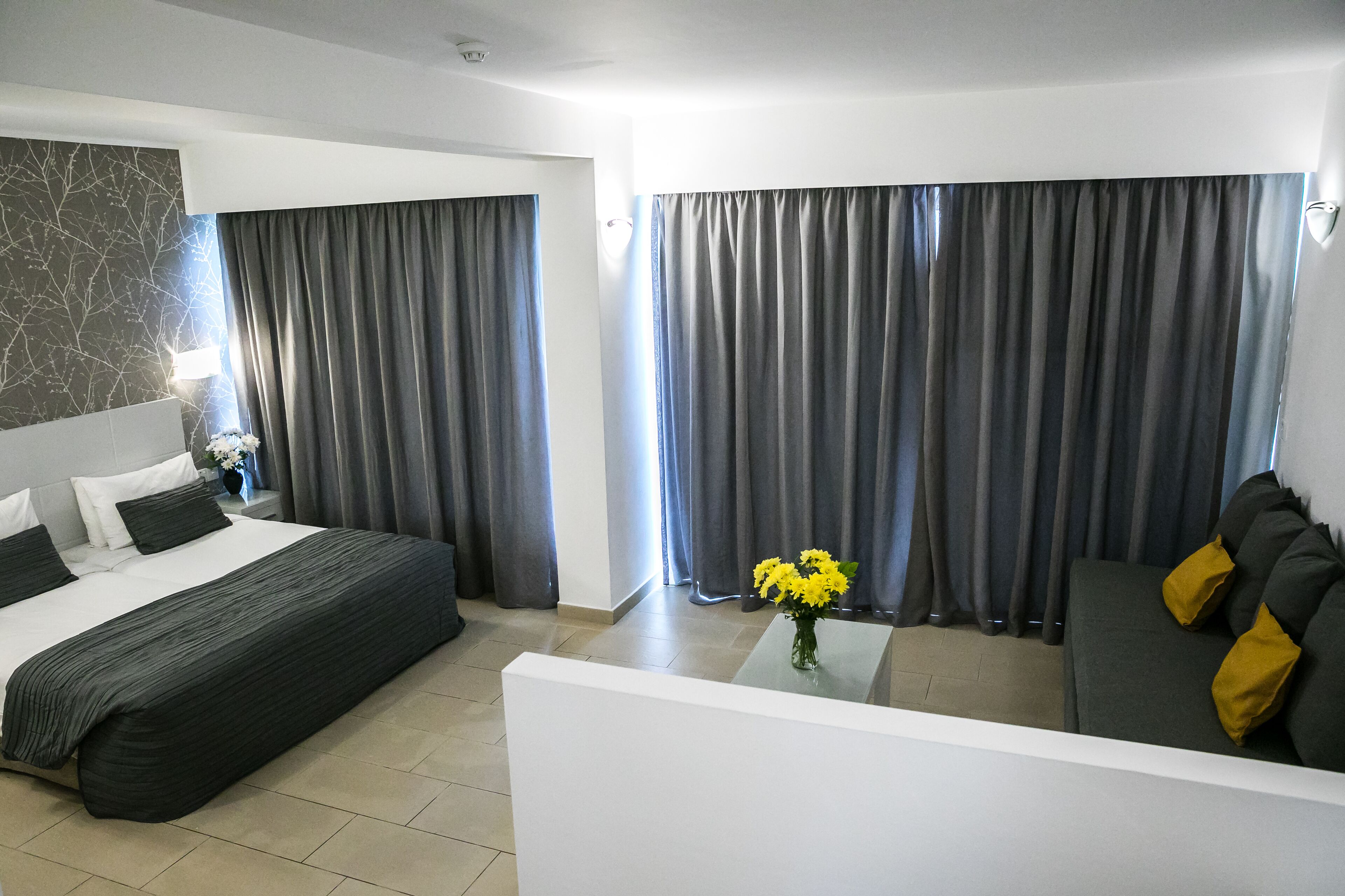 A hotel room with a bed, a sofa, a coffee table with flowers, and curtains.