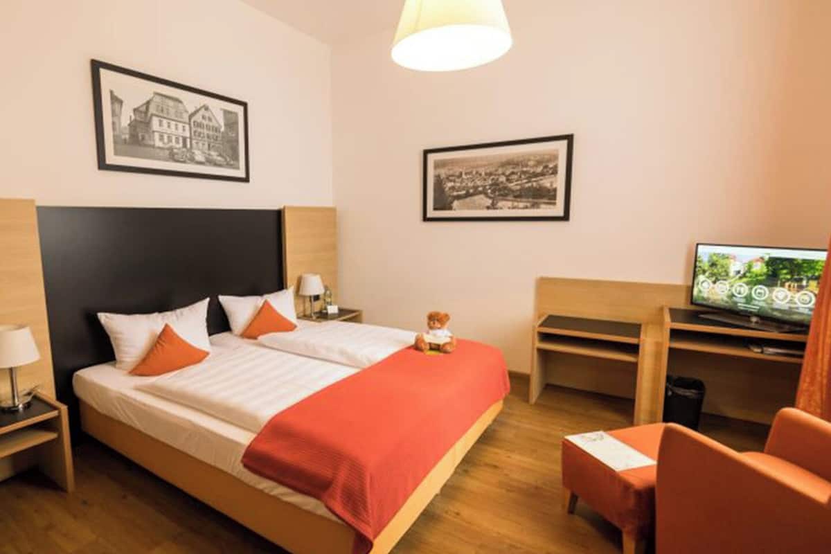 Habitación de hotel con cama, escritorio, silla, televisión y dos cuadros en la pared.