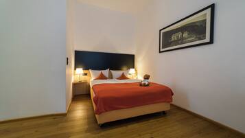 A hotel room with a bed, a nightstand, a lamp, a teddy bear, and a framed picture on the wall.