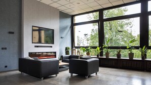 Un salon moderne doté d’une cheminée, de sièges confortables, de grandes fenêtres et de plantes en pot.