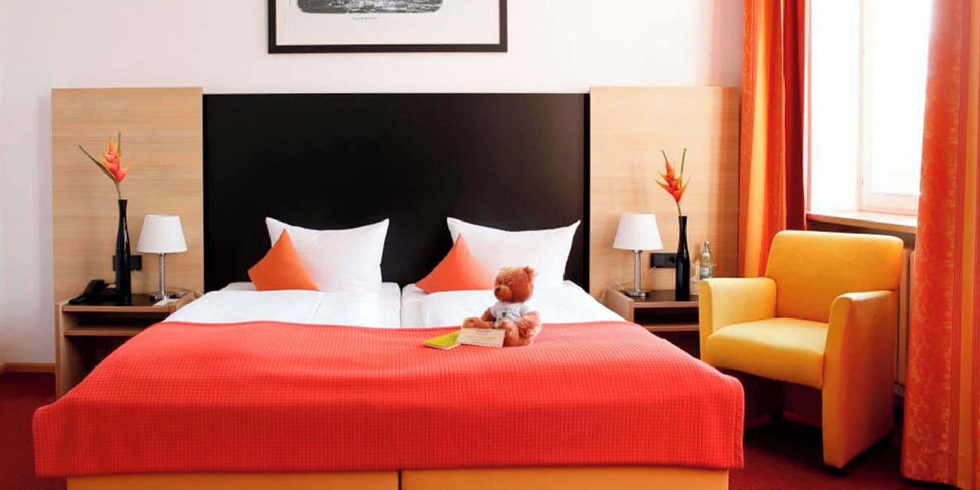 Habitación de hotel con una cama grande, dos mesitas de noche, una silla y una ventana con cortinas.